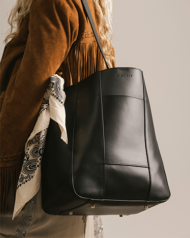 Black leather handbag with a strap over the shoulder, worn by a person in a brown jacket.
