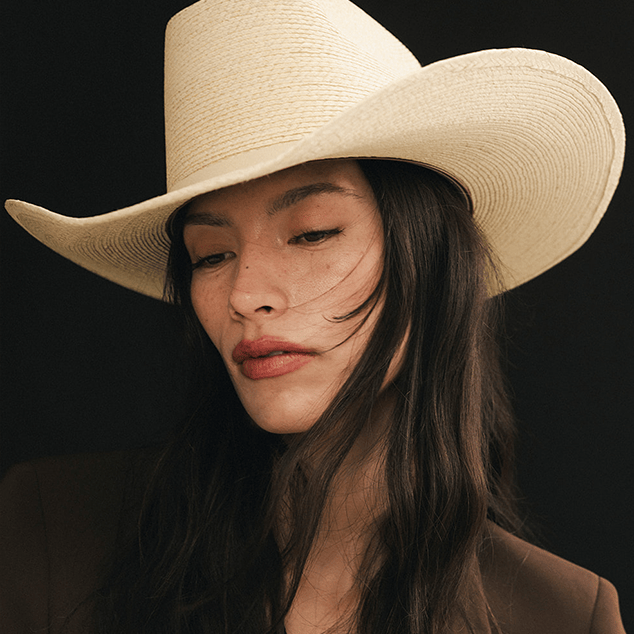 Woman wearing a beige cowboy hat against a black background