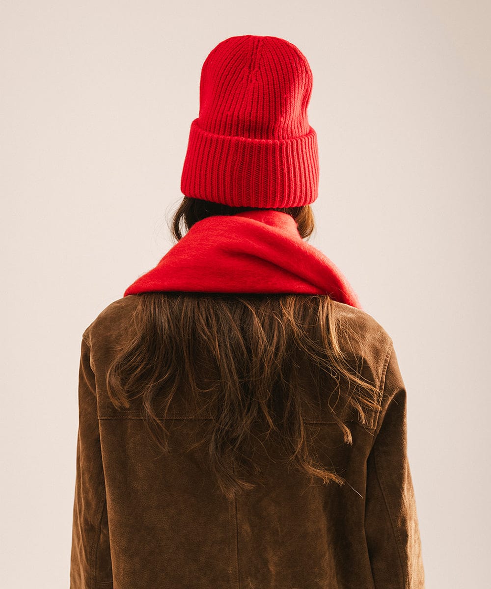 Person wearing a red beanie and scarf with a brown jacket on a plain background #color_red