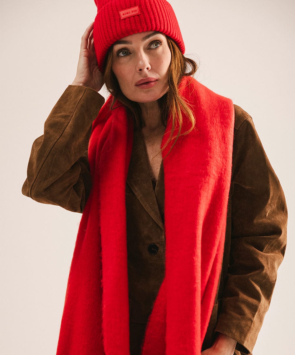 Woman wearing a red beanie and scarf with a brown coat against a plain background #color_red