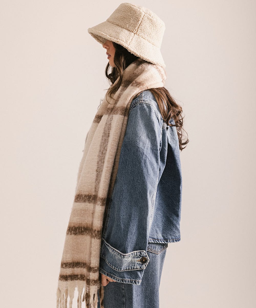 Person wearing a denim jacket, beige bucket hat, and plaid scarf against a plain background #color_ cream - brown plaid