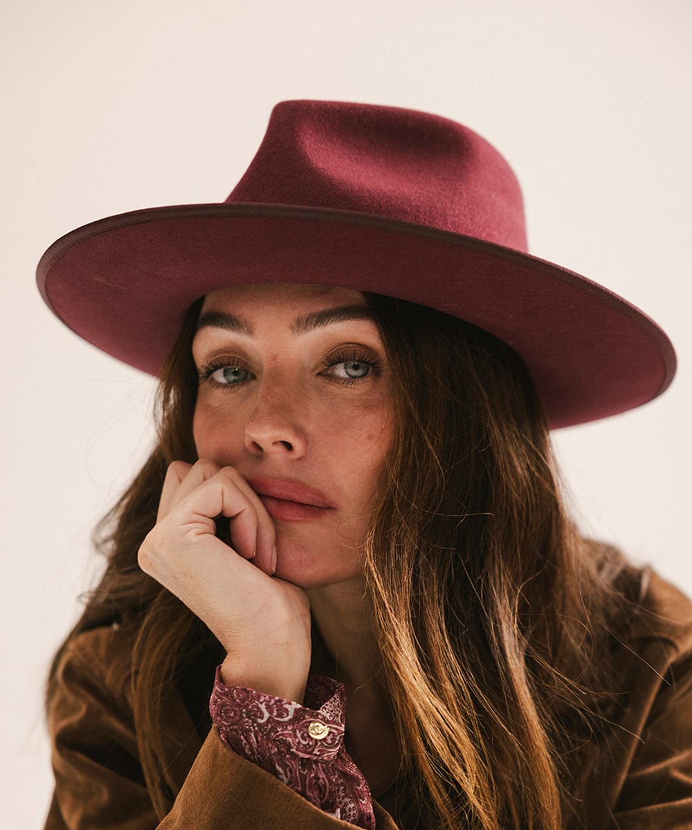 Woman wearing a merlot colored fedora hat and a brown coat against a plain background #color_merlot
