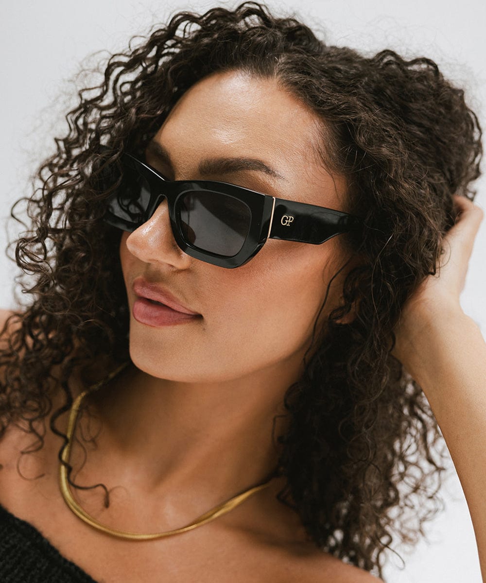 Woman wearing black sunglasses and a gold chain against a plain background #color_black