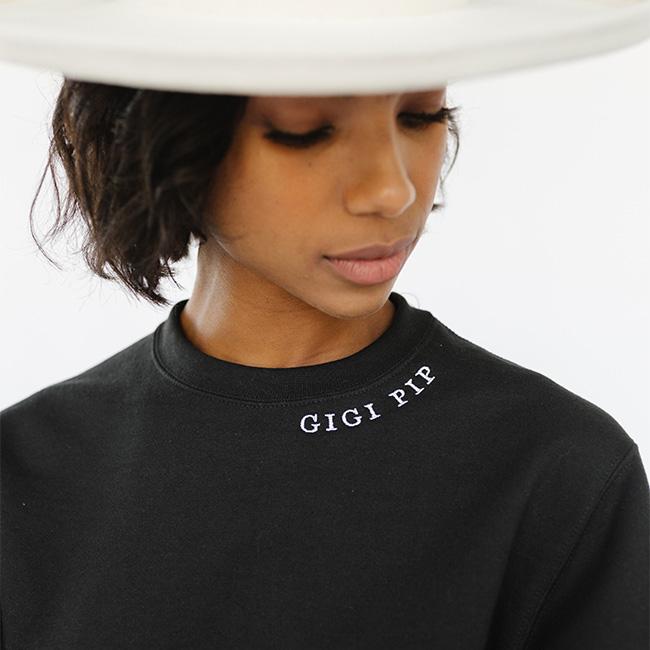 Woman wearing a white hat and a black sweatshirt with the text 'GIGI PIP', looking sideways against a plain background #color_black