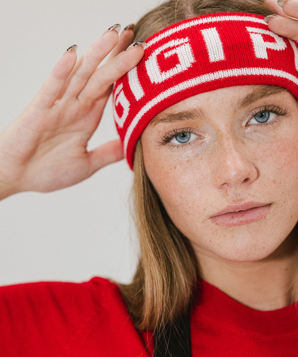 Close up image of a woman wearing a ruby red colored headband with 'GIGI PIP' text and a red t-shirt against a plain background #color_ruby red