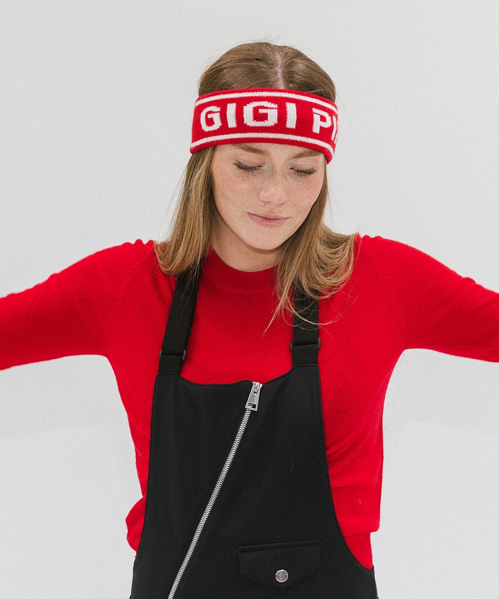 Woman wearing a ruby red colored headband with 'GIGI PIP' text and a red t-shirt with a black sleeveless jacket, looking down against a plain background #color_ruby red