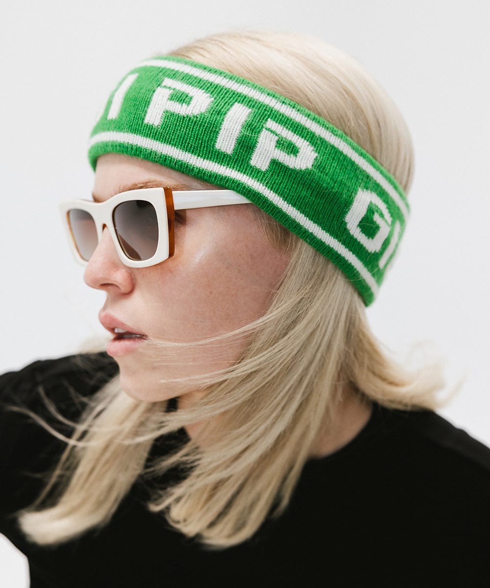 Woman wearing an evergreen colored headband with 'GIGI PIP' text, white sunglasses and a black t-shirt, looking sideways against a plain background #color_evergreen