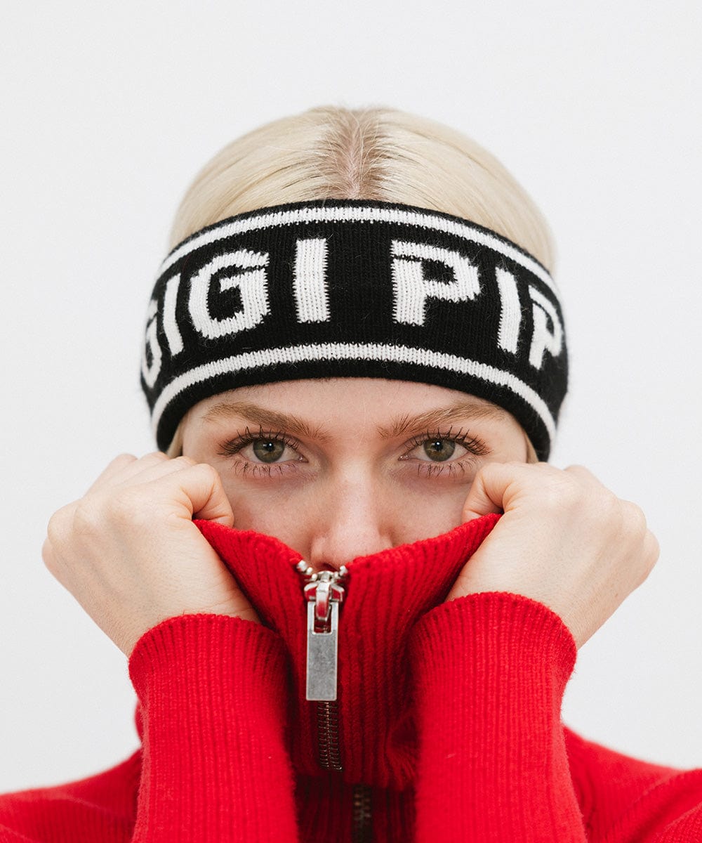 Woman wearing a black headband with 'GIGI PIP' text and a red jacket, covering her face against a plain background #color_black