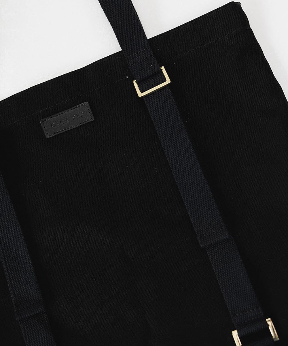 A black canvas tote bag with the brand label and two adjustable straps designed to carry a hat. #color_black