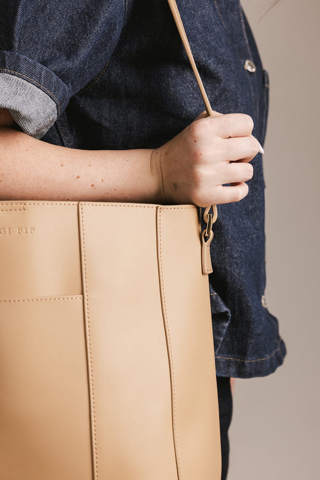 Person wearing a denim shirt carrying a tan Dia everyday leather tote bag against a plain background #color_tan
