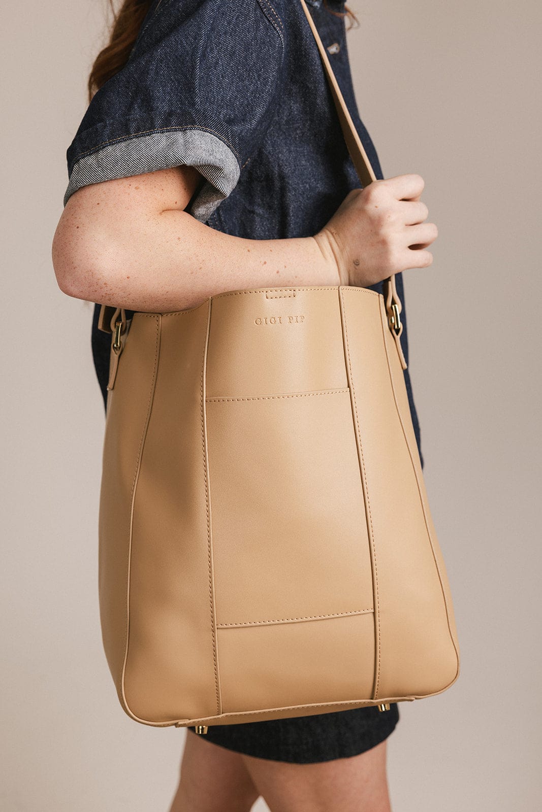 Person wearing a denim shirt and denim skirt carrying a tan Dia everyday leather tote bag against a plain background #color_tan