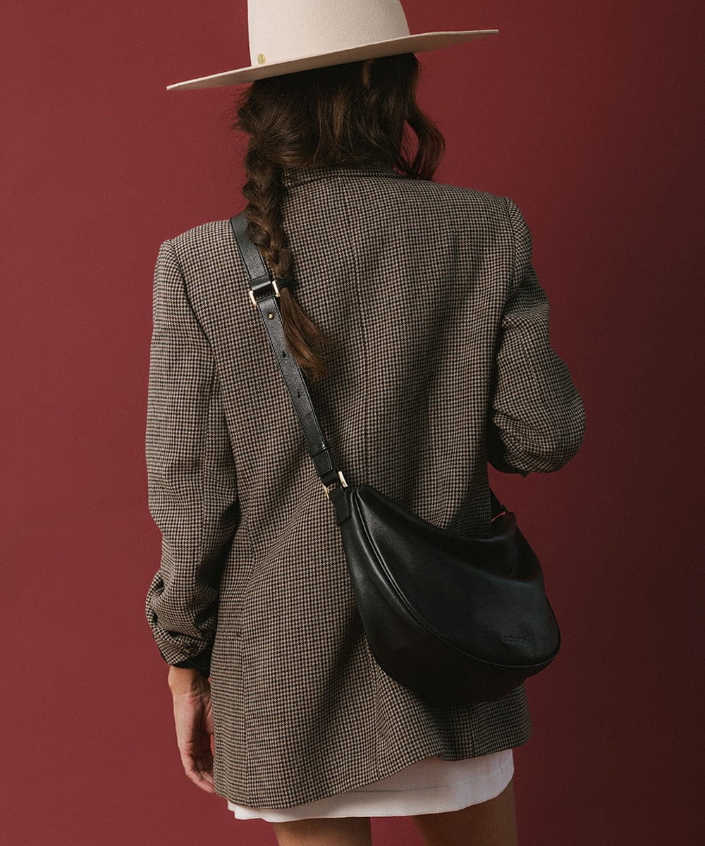 Person wearing a white hat and a coat, carrying a black genuine leather slouchy bag against a maroon background #color_black