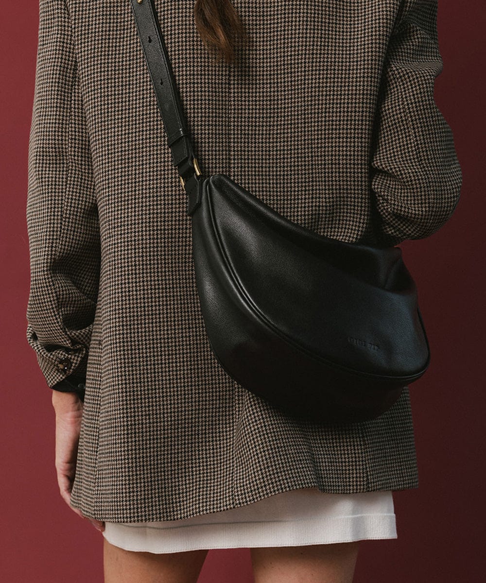 Person wearing a coat carrying a black genuine leather slouchy bag against a maroon background #color_black