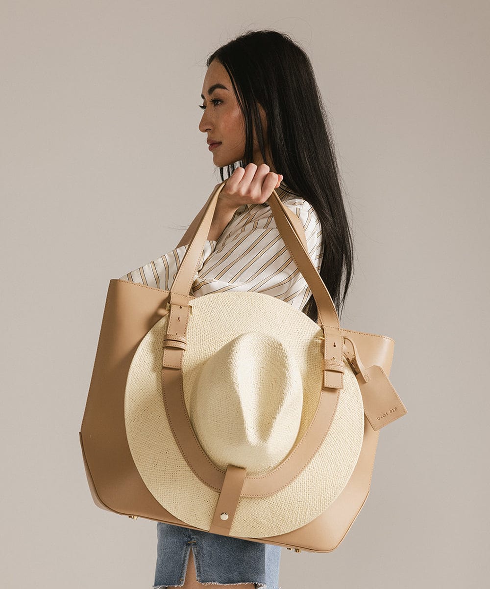 Woman carrying a beige Hayes Hat Carrying Tote bag with a white cowboy hat against a plain background #color_tan