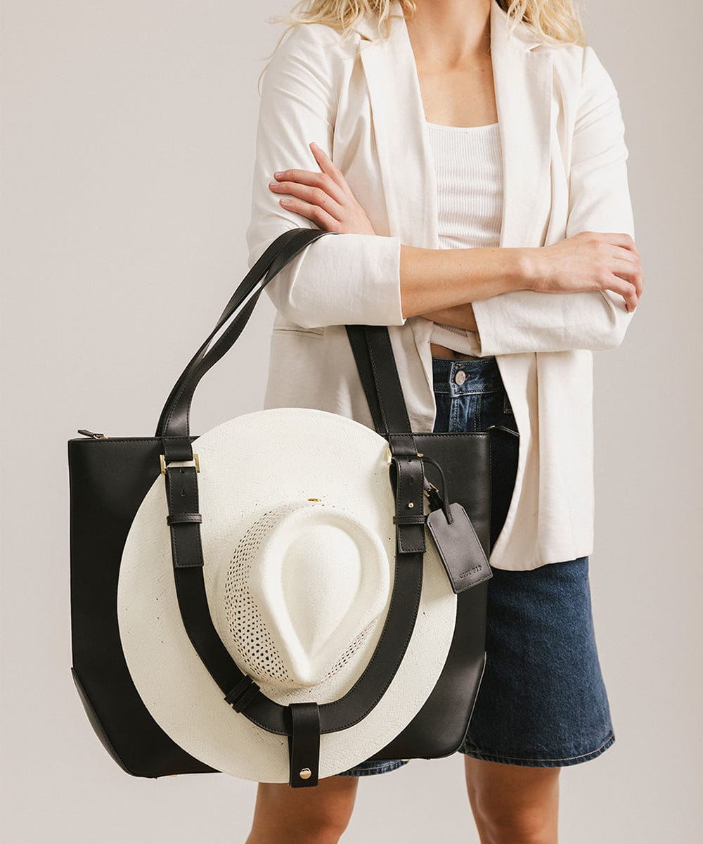 Person carrying a black Hayes Hat Carrying Tote bag with a white cowboy hat against a plain background #color_black