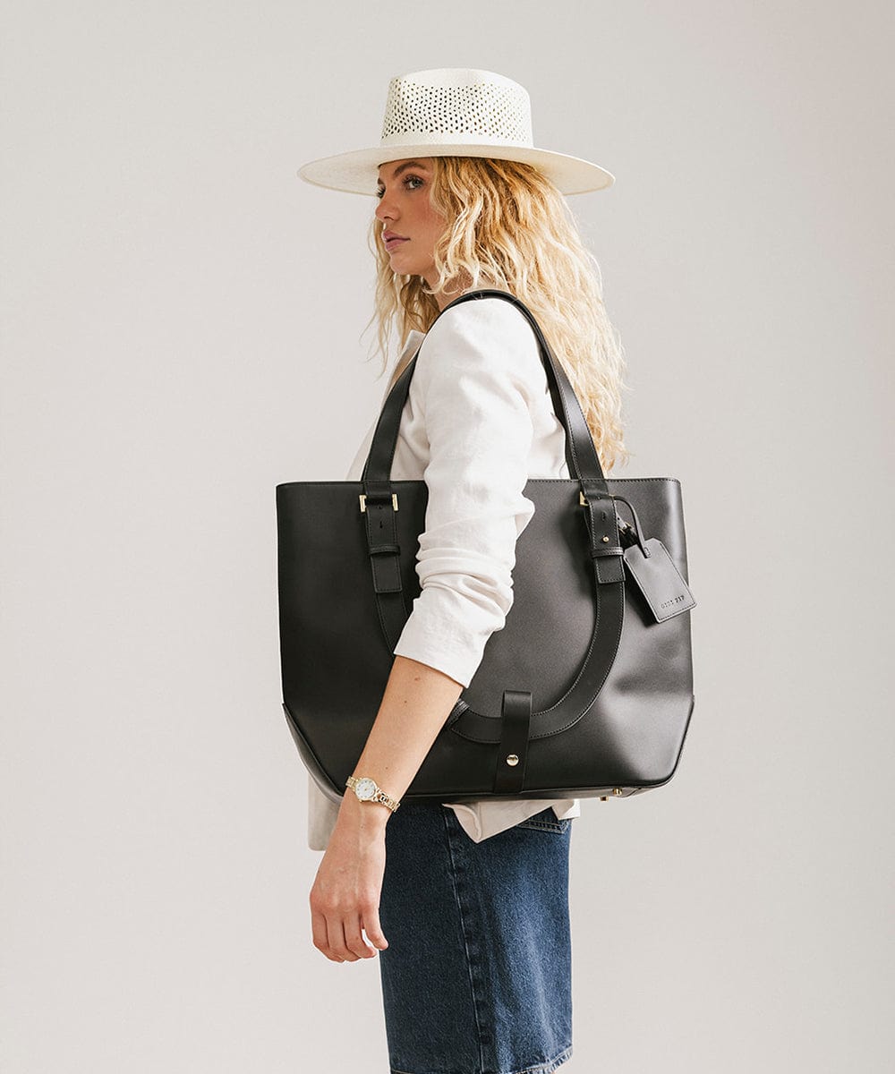 Woman carrying a black Hayes Hat Carrying Tote bag against a plain background #color_black
