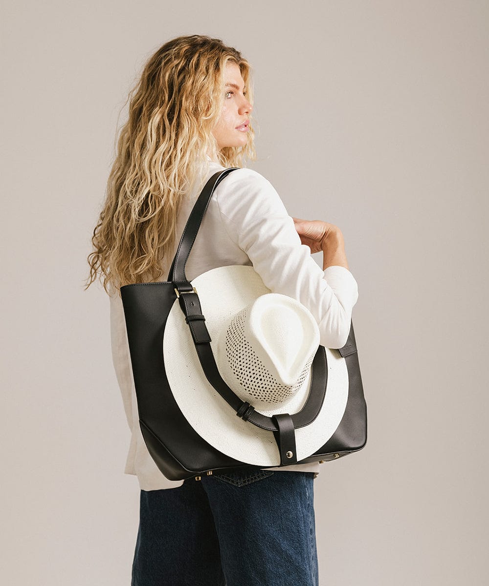 Woman carrying a black Hayes Hat Carrying Tote bag with a white cowboy hat against a plain background #color_black
