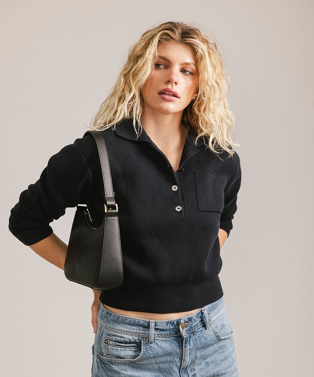 Woman wearing a black shirt and blue jeans, carrying a black genuine leather handbag against a plain background #color_black