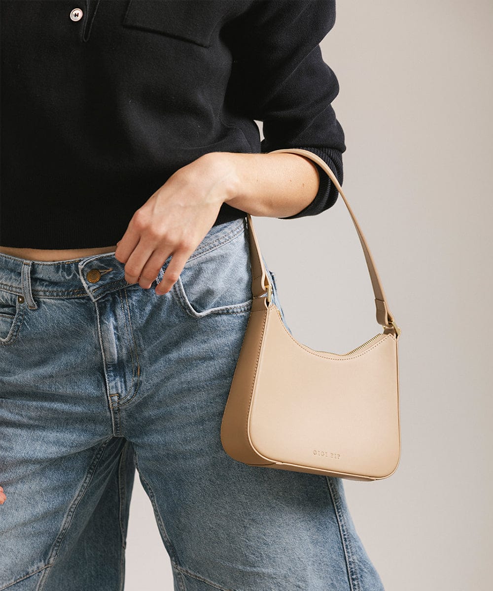 Person wearing a black shirt and denim shorts, carrying a tan genuine leather handbag against a plain background #color_tan