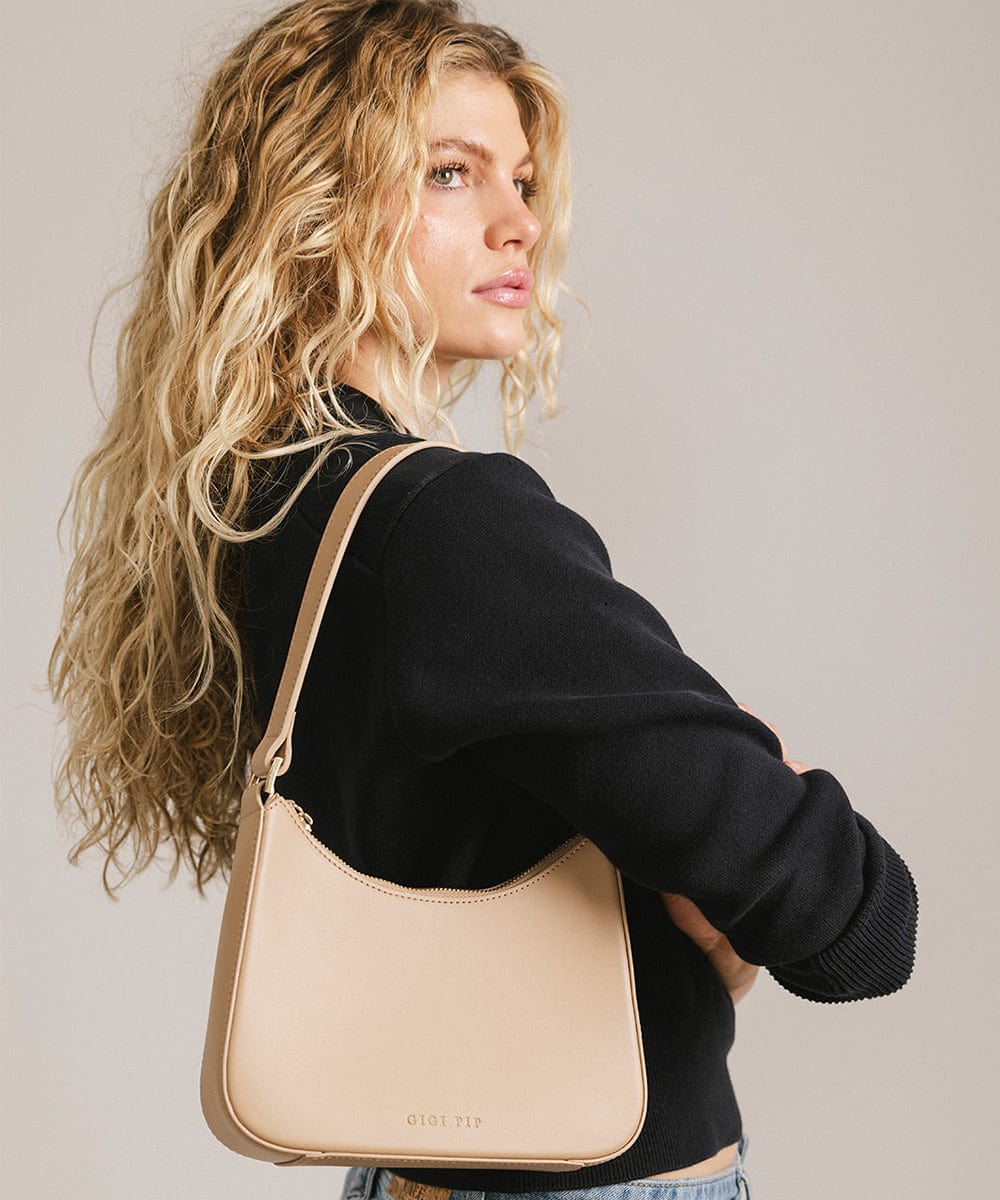 Woman wearing a black shirt, carrying a tan genuine leather handbag against a plain background #color_tan