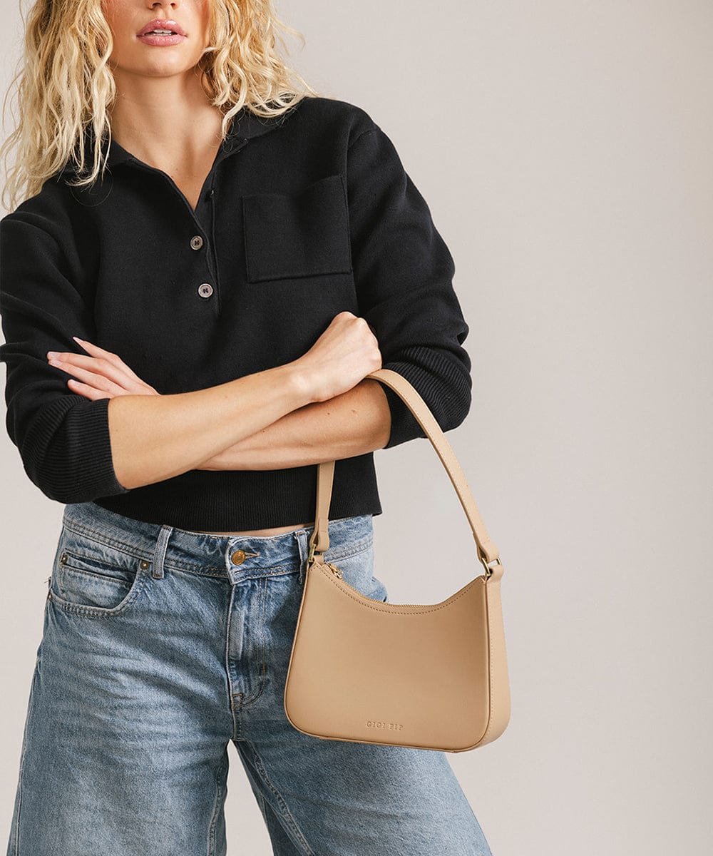 Person wearing a black shirt and denim shorts, carrying a tan genuine leather handbag against a plain background #color_tan