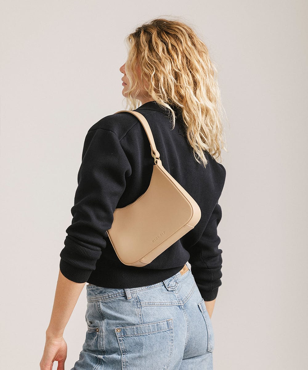 Person wearing a black shirt and denim shorts, carrying a tan genuine leather handbag, facing sideways against a plain background #color_tan