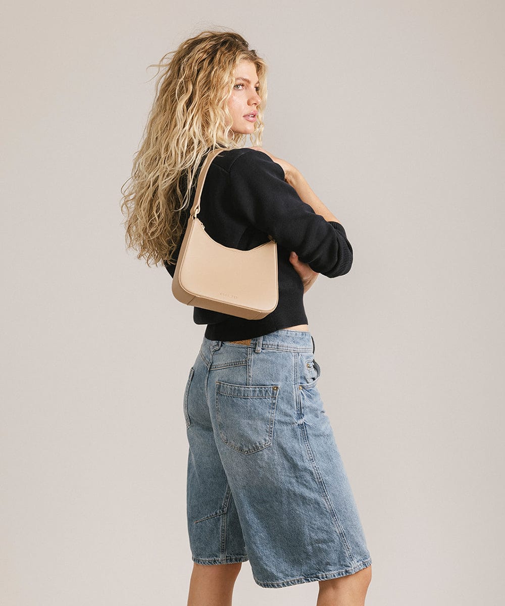 Woman wearing a black shirt and denim shorts, carrying a tan genuine leather handbag against a plain background #color_tan
