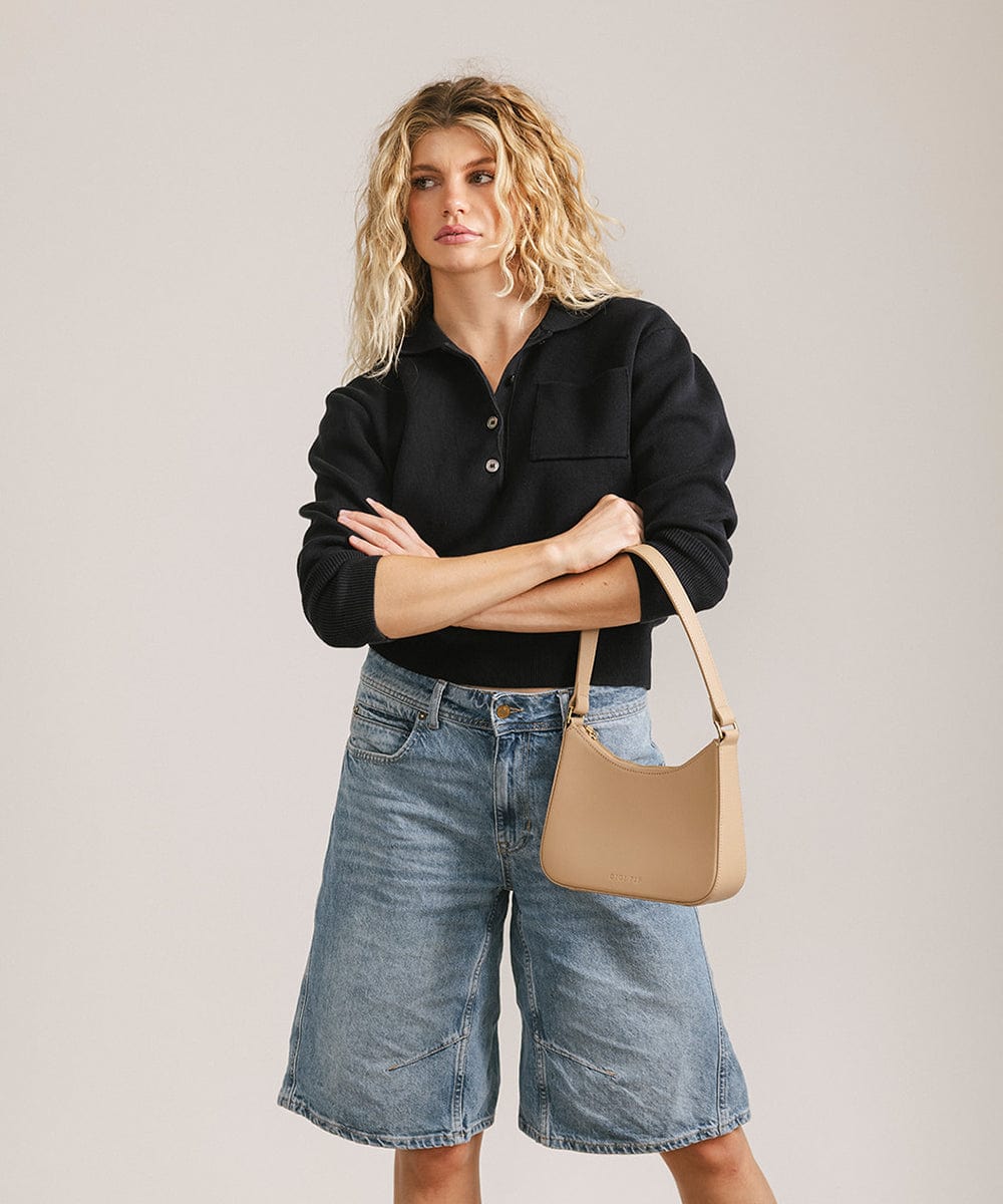 Woman wearing a black shirt and denim shorts, carrying a tan genuine leather handbag against a plain background #color_tan