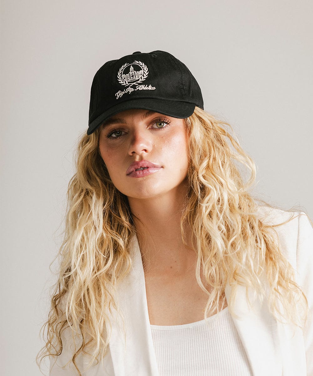 Woman wearing a black ball cap with a white logo and text and a white blazer against a plain background #color_black