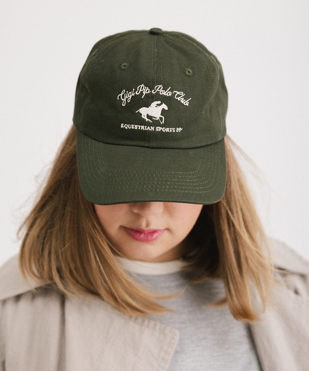 Woman wearing a dark green cap with white text and horse logo against a plain background #color_dark green