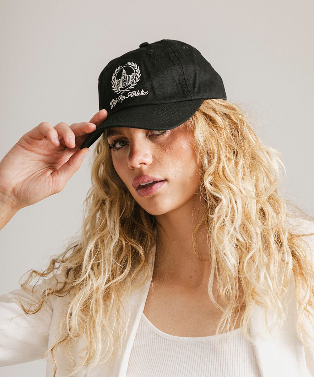 Woman wearing a black ball cap with a white logo and text and a white blazer, posing against a plain background #color_black