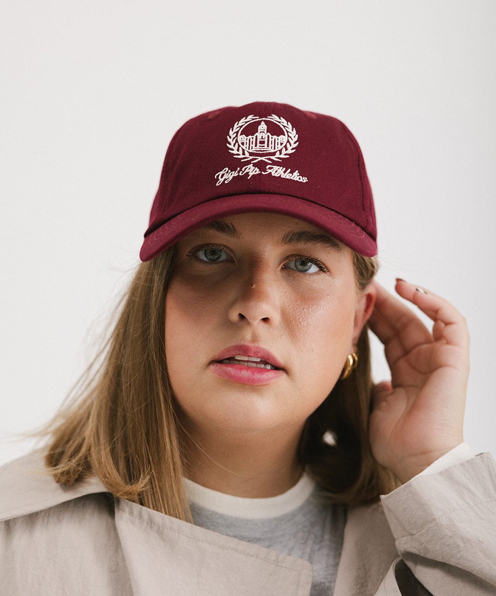 Woman wearing a burgundy ball cap with a white logo and text against a plain background #color_burgundy