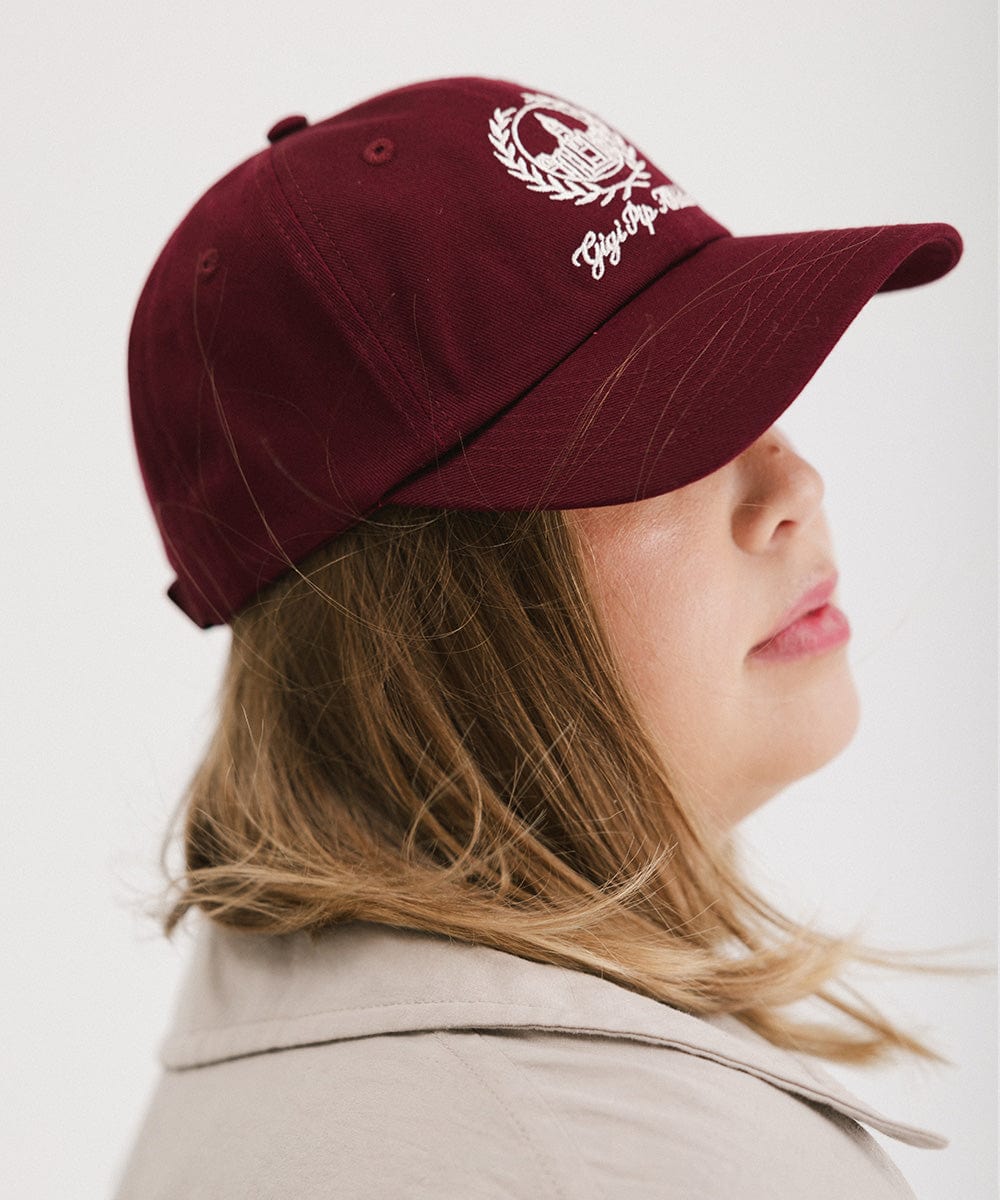 Woman wearing a burgundy ball cap with a white logo and text facing sideways against a plain background #color_burgundy