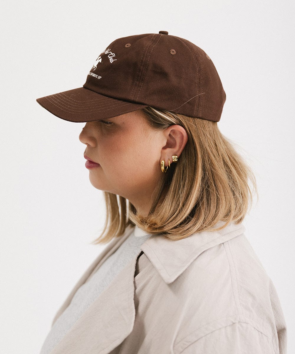 Woman wearing a brown cap and a beige jacket, facing sideways against a plain background #color_chocolate