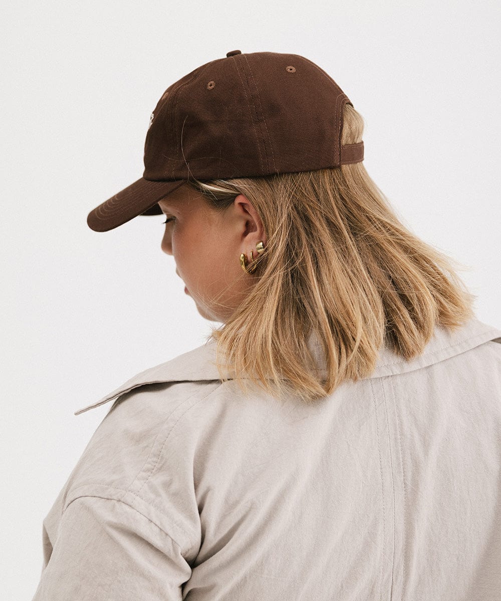 Woman wearing a brown cap and a beige jacket, facing behind against a plain background #color_chocolate