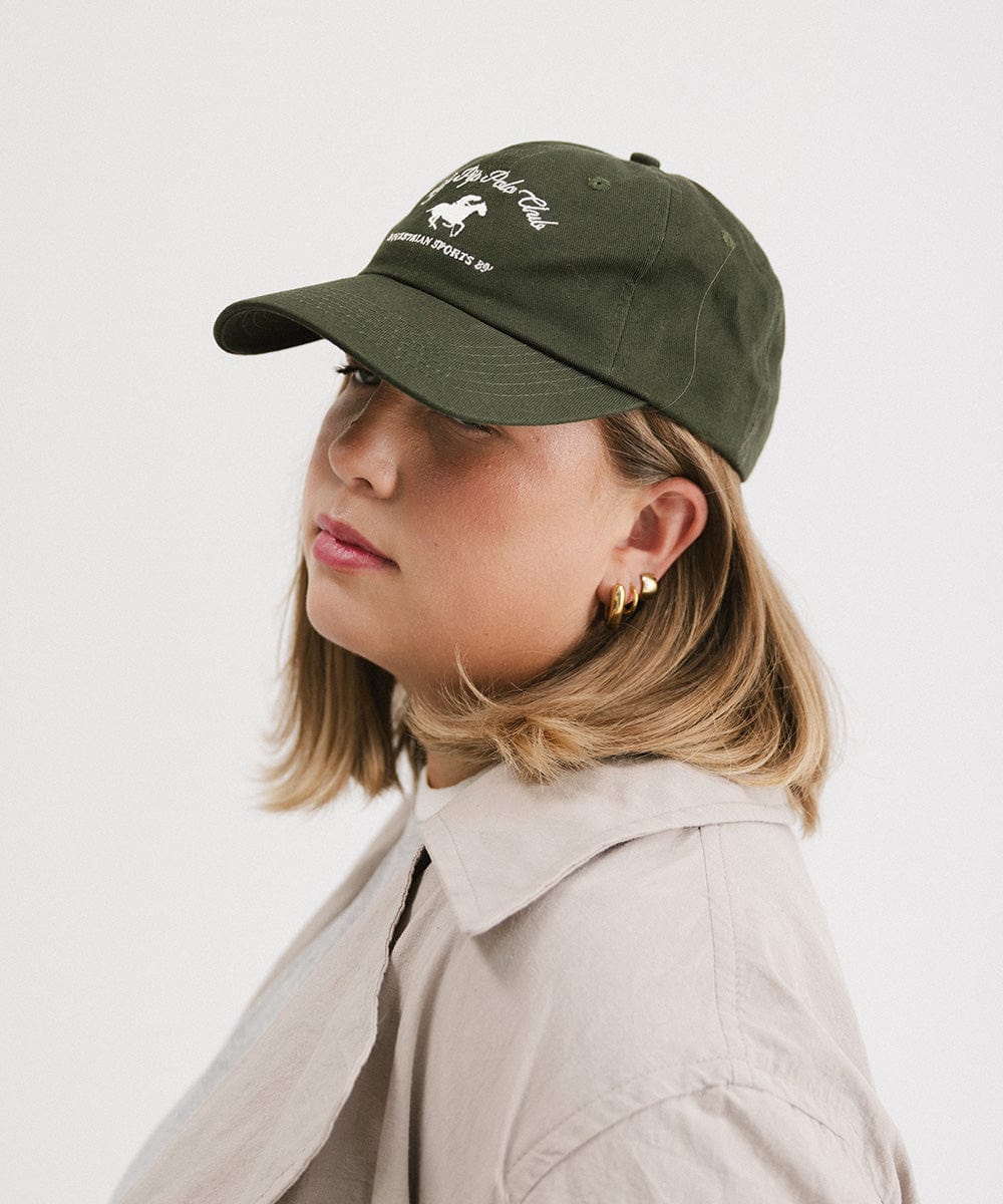 Woman wearing a dark green cap with white text and horse logo and a beige shirt, posing sideways against a plain background #color_dark green