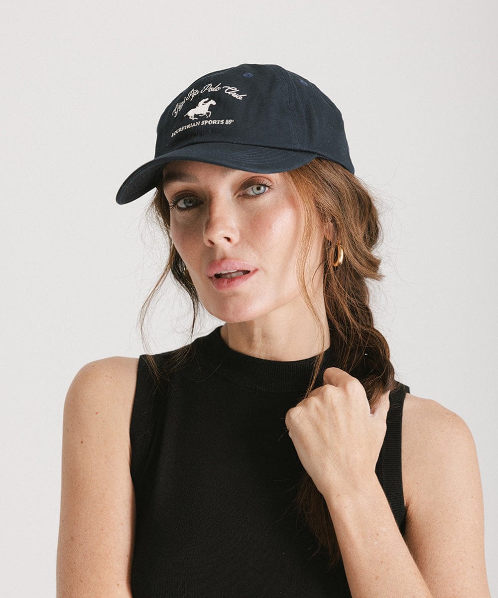 Woman wearing a navy cap with white text and horse logo and a black top against a plain background #color_navy