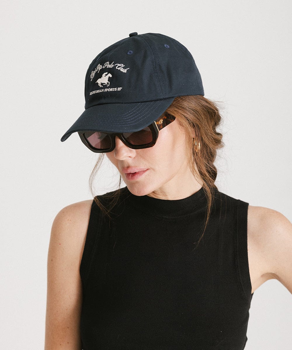Woman wearing a navy cap with white text and horse logo, sunglasses, and a black top against a plain background #color_navy