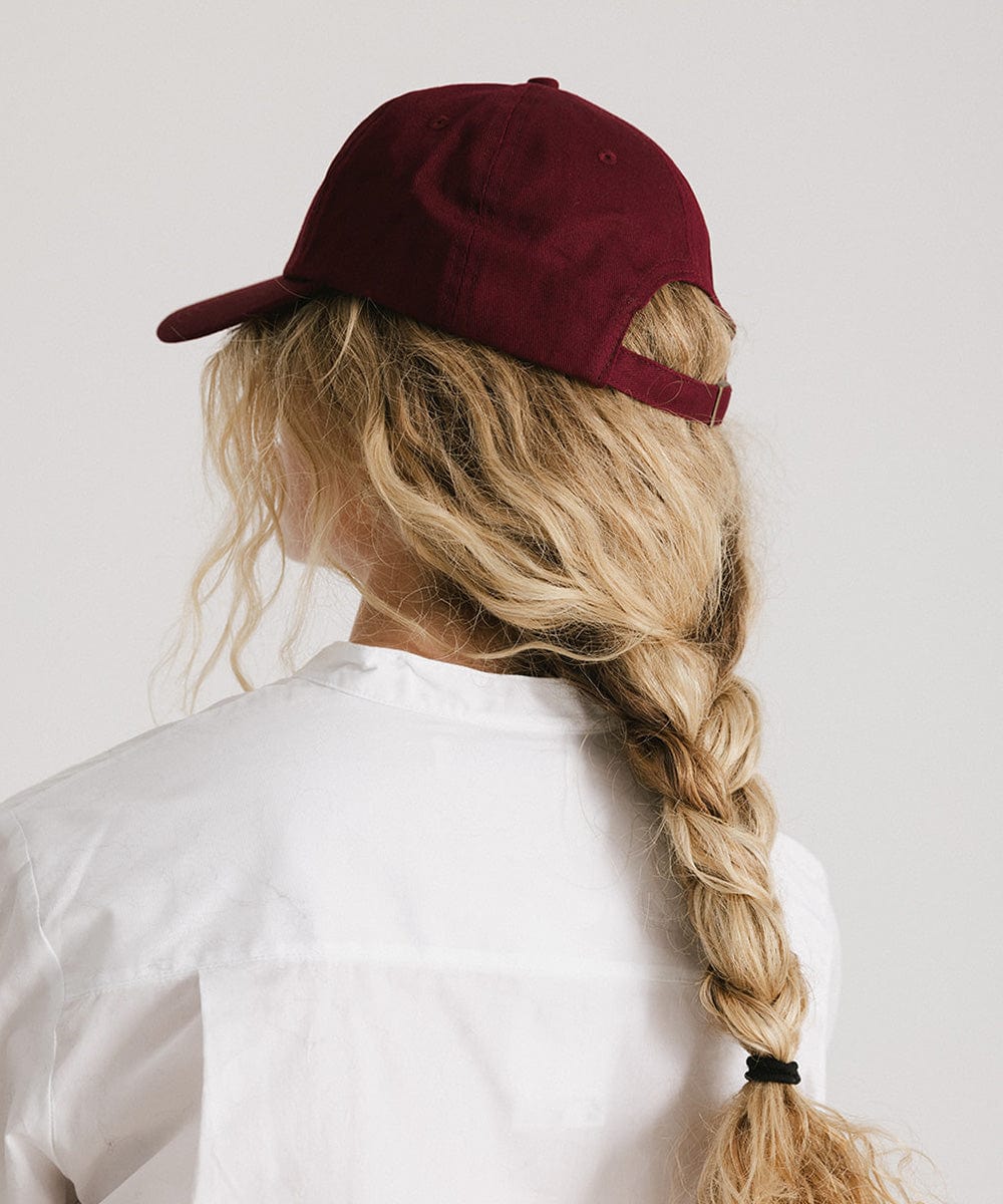 Woman wearing a burgundy cap and a white shirt, facing behind against a plain background #color_burgundy