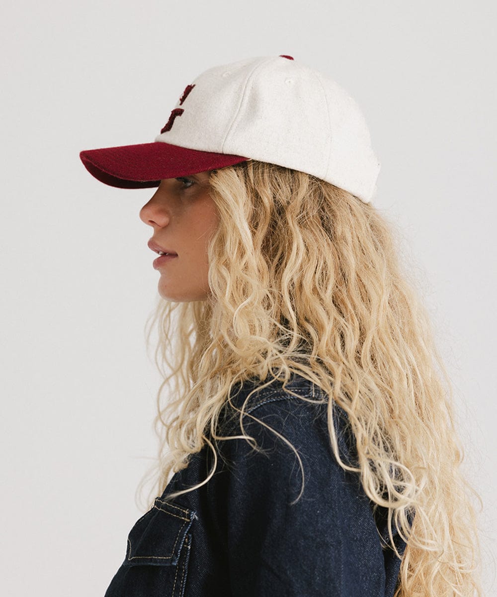 Woman wearing a white and burgundy baseball cap and a denim shirt, facing sideways against a plain background #color_burgundy