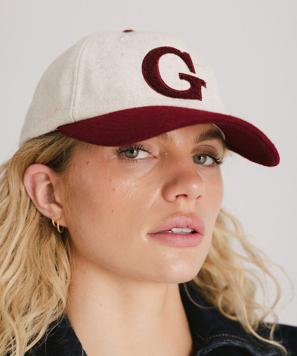Woman wearing a white and burgundy baseball cap with the letter 'G' against a plain background #color_burgundy