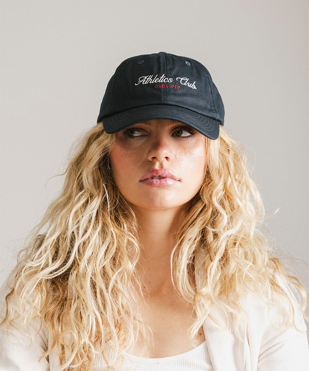 Woman with long hair wearing a navy cap with white 'Athletics Club' text against a plain background #color_navy