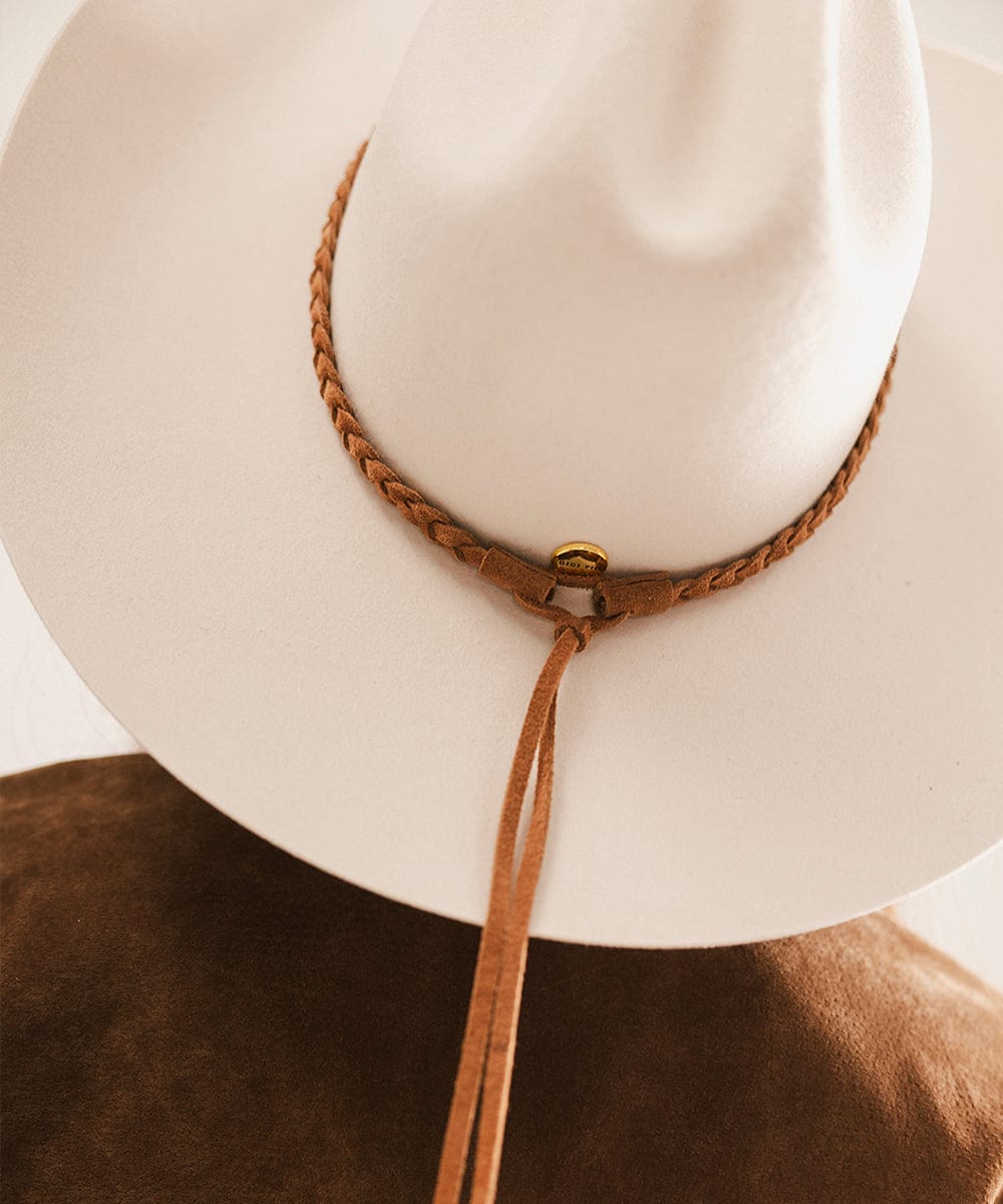 White cowboy hat with a brown leather strap on a blurred background #color_caramel