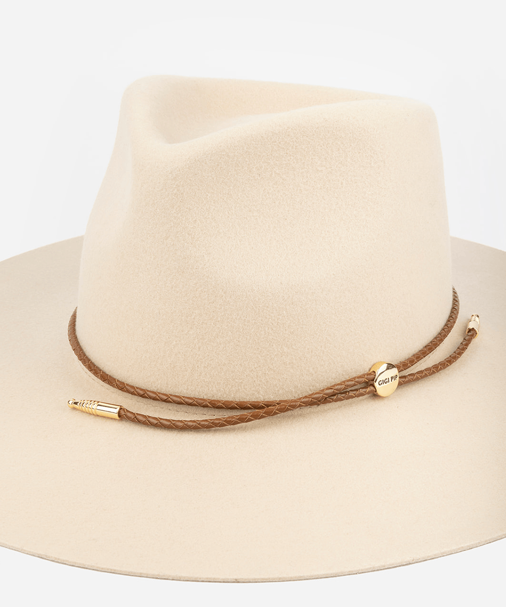 Beige fedora hat with brown leather thin braided wrap band strap and gold hardware on a white background #color_cognac