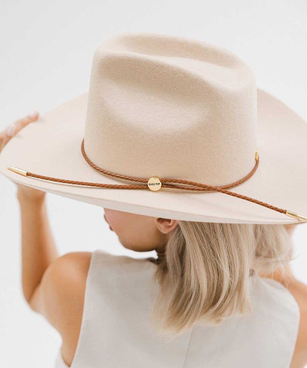 Woman wearing a cream cowboy hat with a cognac colored braided hat band and a white top, posing against a plain background #color_cognac