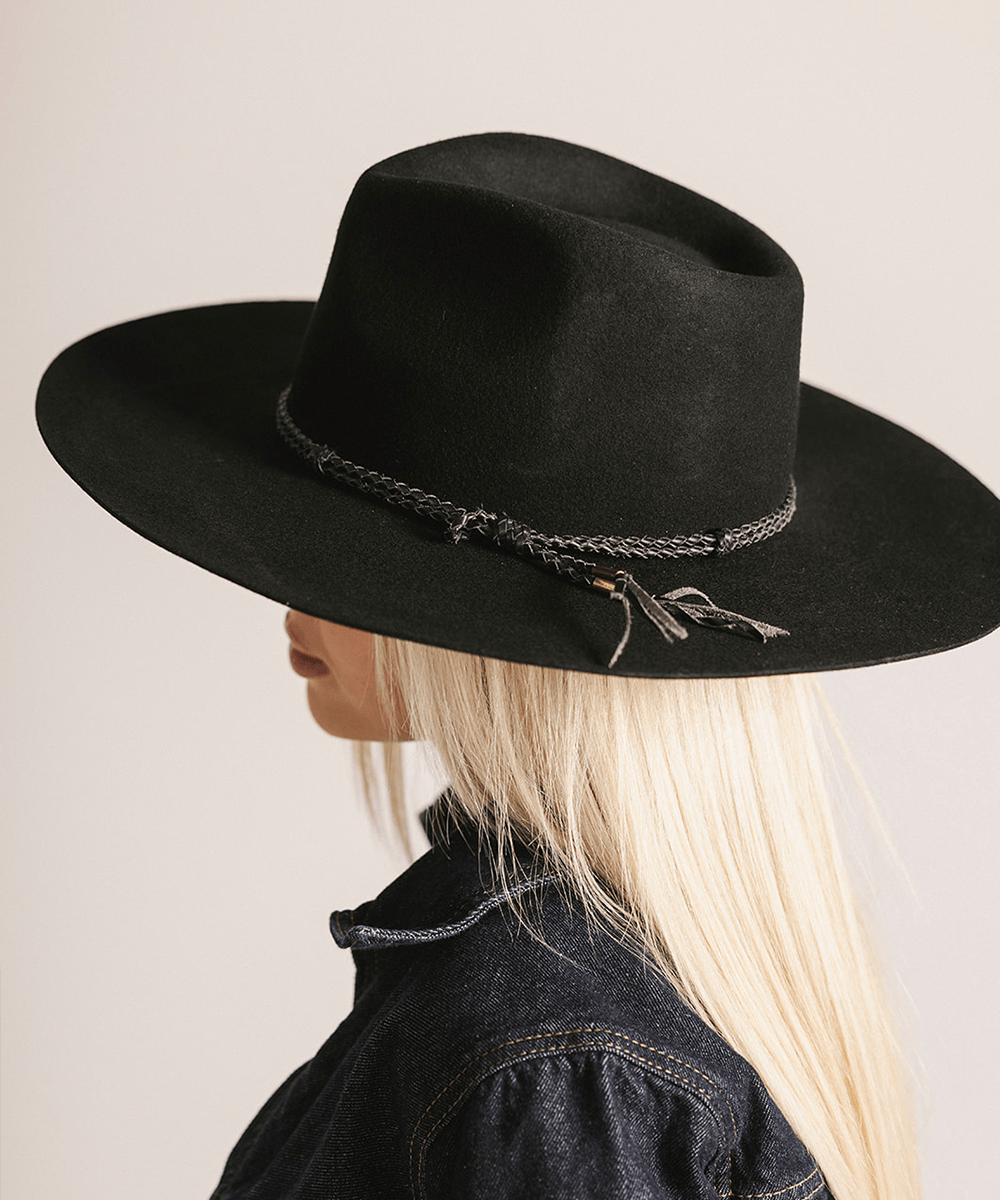 Person wearing a black wide-brimmed hat with decorative band on a neutral background #color_black