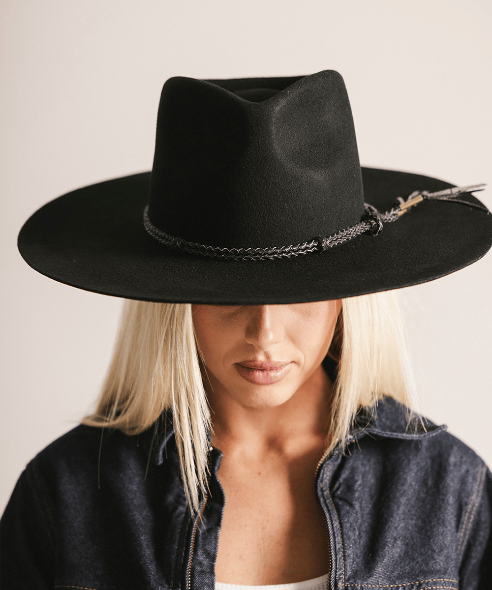 Person wearing a black wide-brimmed hat with decorative elements on a plain background #color_black