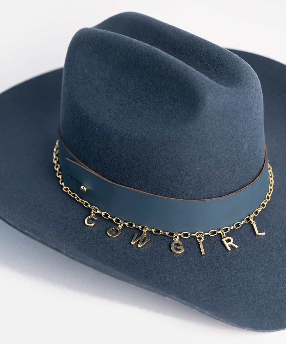 A blue cowboy hat with a gold chain hat band and gold letter hat charms making up the word 'COWGIRL' on a plain background #color_gold