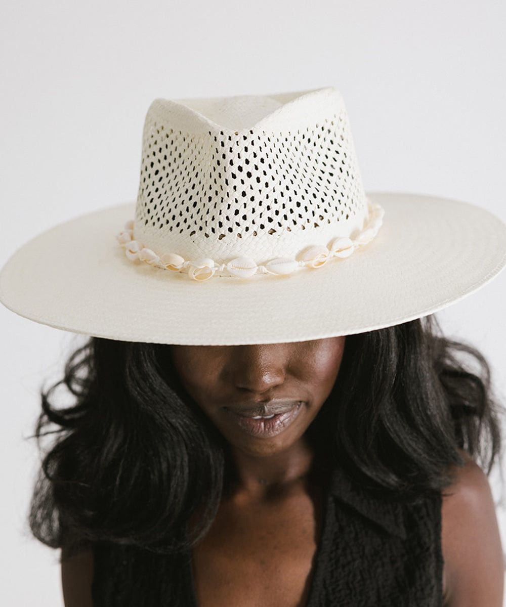 Woman wearing a white hat with a white shell hat band and a black top against a plain background #color_natural