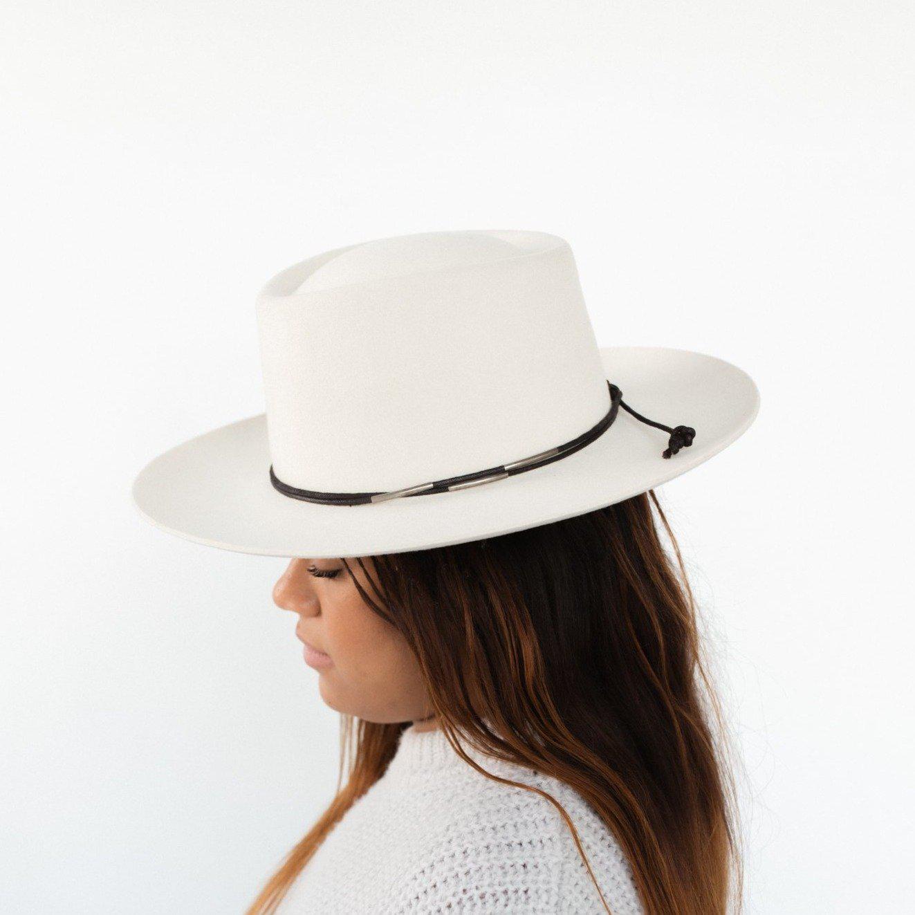 Woman wearing a white hat with a black rope band with beads and a white sweater, facing sideways against a plain background #color_black